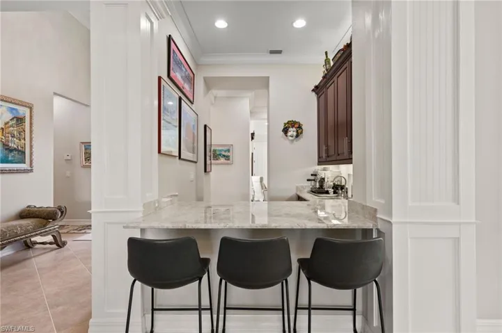 Kitchen featuring a breakfast bar, light stone counters, light tile patterned flooring, kitchen peninsula, and dark brown cabinetry