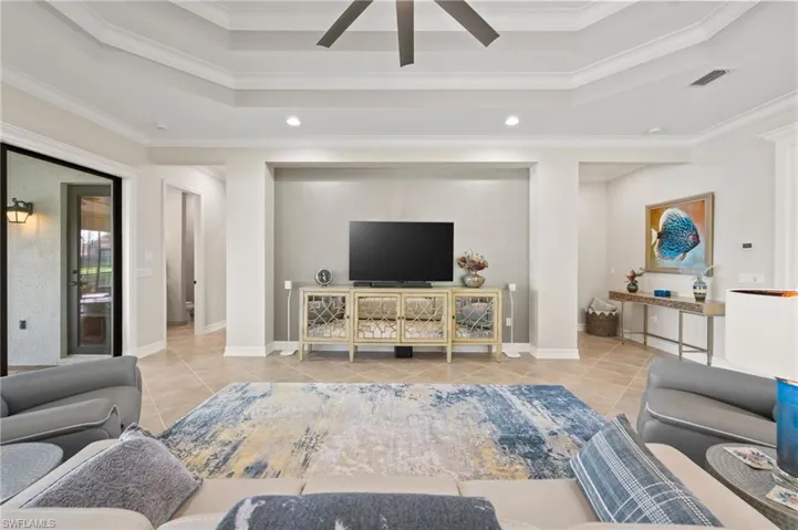 Living room with crown molding, light tile patterned floors, ceiling fan, and a raised ceiling