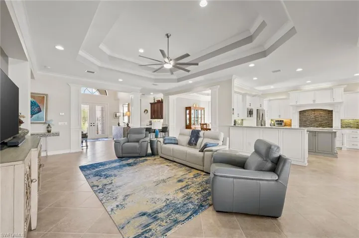 Living room featuring ornamental molding, a tray ceiling, ceiling fan, and light tile patterned floors