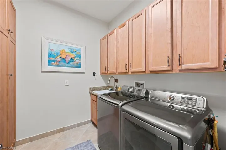 Laundry room featuring light tile patterned floors, cabinets, sink, and washer and dryer