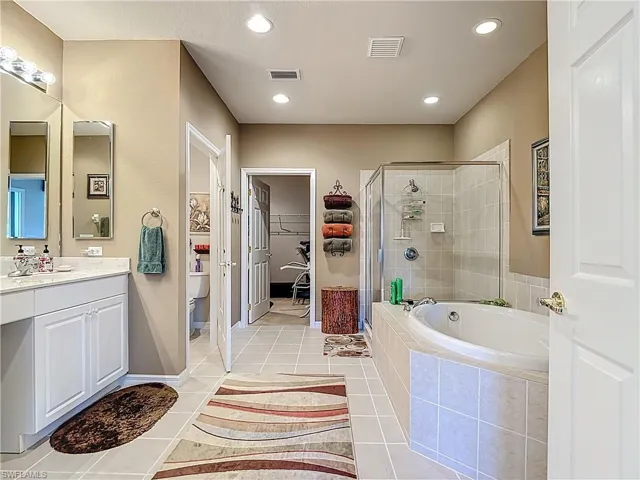 Full bathroom with a spacious closet, a stall shower, a garden tub, vanity, and light tile patterned floors