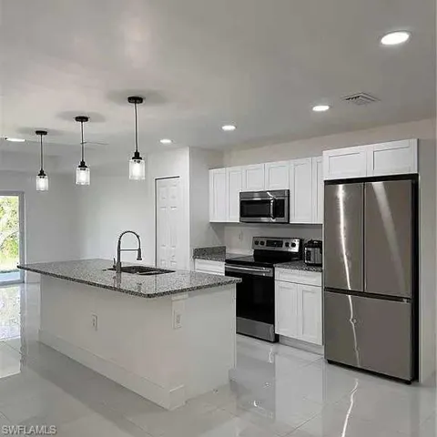 Kitchen with stone counters, visible vents, appliances with stainless steel finishes, white cabinetry, and a sink