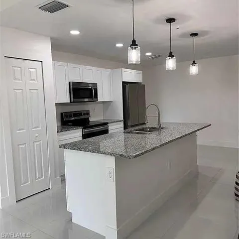 Kitchen featuring visible vents, dark stone counters, appliances with stainless steel finishes, white cabinetry, and a sink