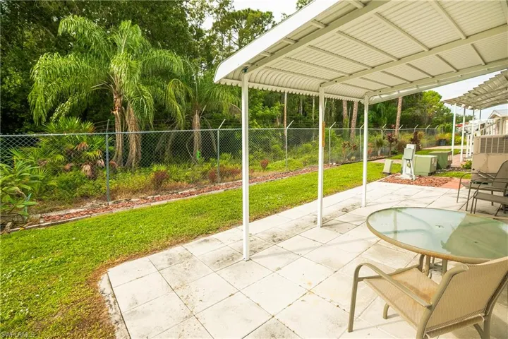 Covered patio with square tile flooring, bordered by a chain-link fence and green lawn