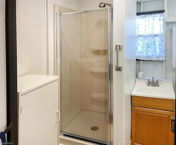Shower stall featuring a glass enclosure with a chrome frame and a wall-mounted grab bar, accompanied by a wood-finish vanity with a single-basin countertop and a dual-handle chrome faucet