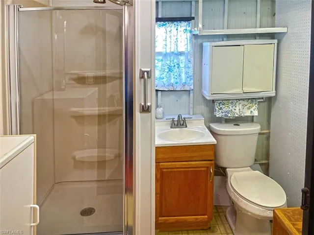 Glass-enclosed shower stall with integrated shelving, wood-finish vanity cabinet, porcelain sink, and wall-mounted storage cabinet