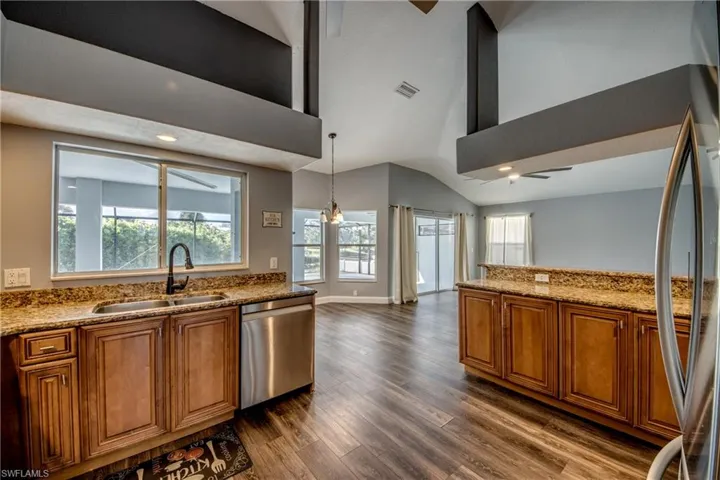 Kitchen with wood finish cabinets, a ceiling fan, light stone countertops, stainless steel appliances, and dark wood-type flooring