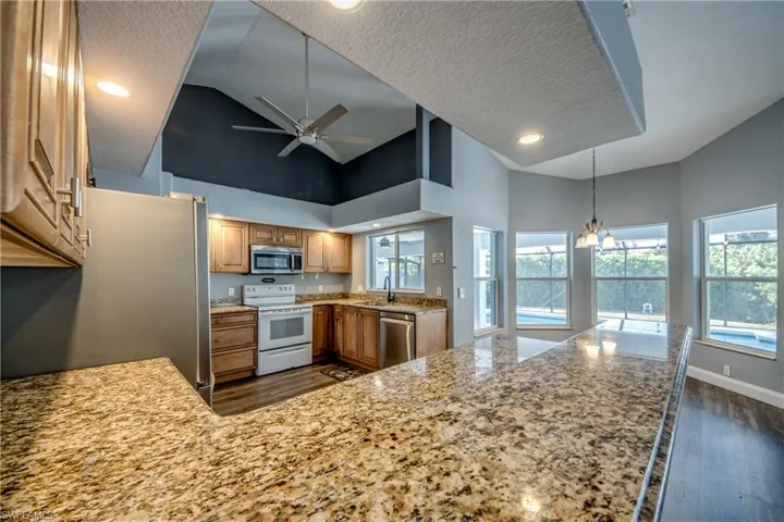 Kitchen featuring stainless steel appliances, suspended lighting, dark wood-type flooring, ceiling fan, and a high textured ceiling