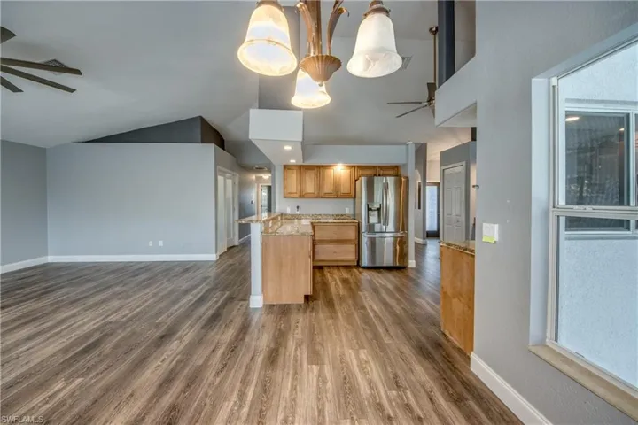 Kitchen featuring a ceiling fan, open floor plan, stainless steel refrigerator with ice dispenser, dark wood-type flooring, and lofted ceiling