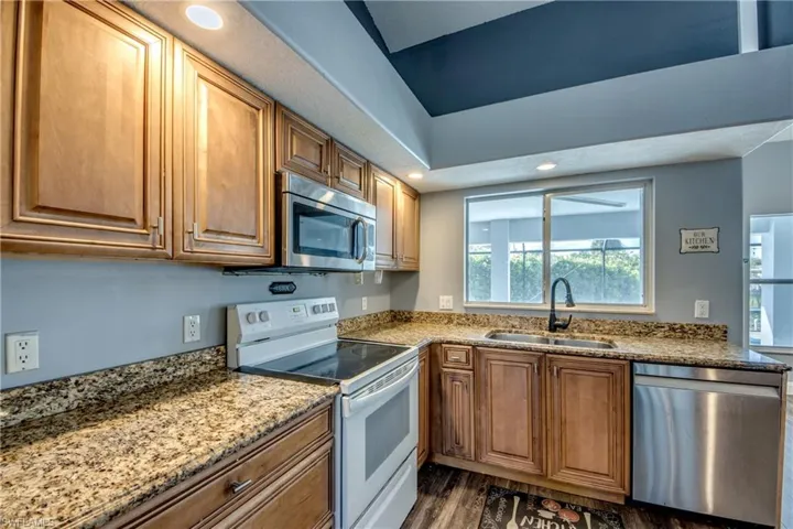 Kitchen featuring stainless steel appliances, light stone countertops, wood finish cabinets, dark wood-style floors, and recessed lighting