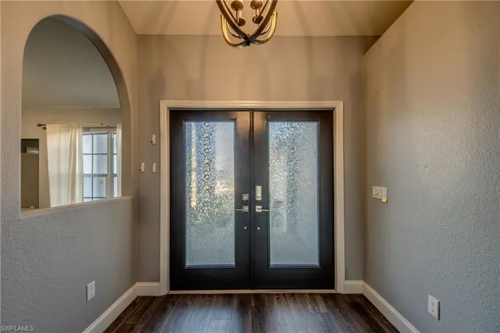 Foyer featuring a textured wall, french doors, dark wood finished floors, a chandelier, and arched walkways