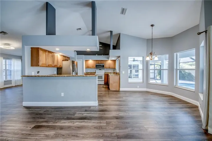 Kitchen with suspended lighting, stainless steel appliances, open floor plan, wood finish cabinetry, and a peninsula