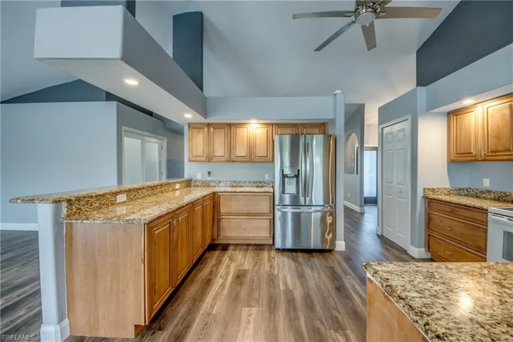Kitchen featuring stainless steel fridge, light stone counters, dark wood finished floors, vaulted ceiling, and a peninsula