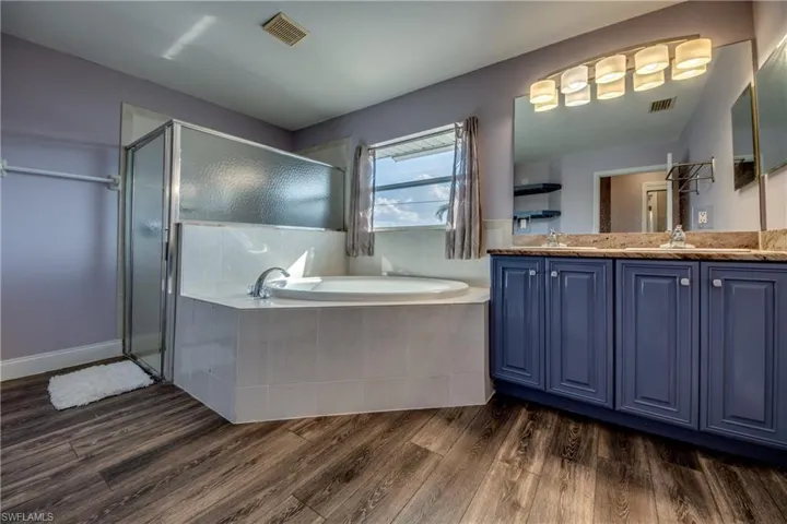 Bathroom with double vanity, a garden tub, a stall shower, and dark wood finished floors