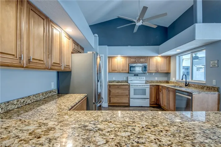 Kitchen with a ceiling fan, stainless steel appliances, light stone counters, wood finish cabinetry, and vaulted ceiling