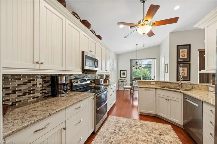 Kitchen featuring appliances with stainless steel finishes, decorative backsplash, dark wood-type flooring, light stone counters, and vaulted ceiling