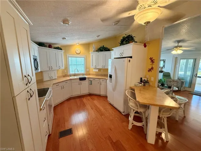 Kitchen featuring white appliances, light countertops, light wood-style floors, white cabinets, and lofted ceiling