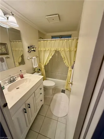 Bathroom featuring vanity, light tile patterned floors, a textured ceiling, crown molding, and shower / tub combo with curtain