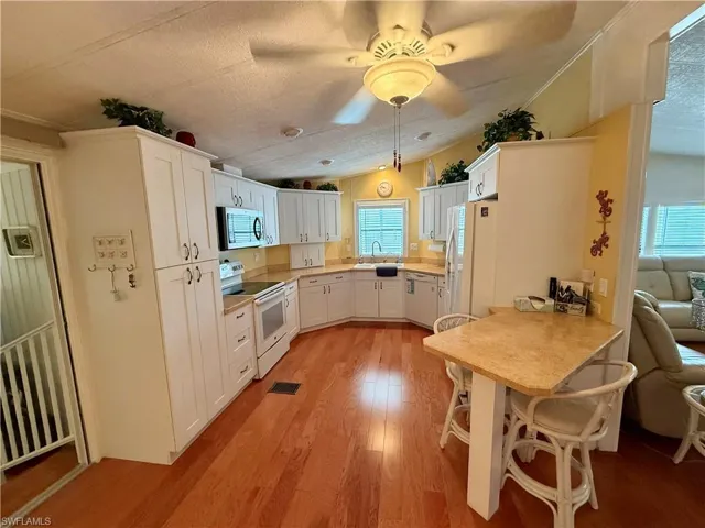 Kitchen featuring light countertops, lofted ceiling, white appliances, light wood finished floors, and white cabinetry