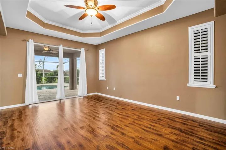 Master bedroom featuring ornamental molding, ceiling fan, a raised ceiling, and vinyl flooring.