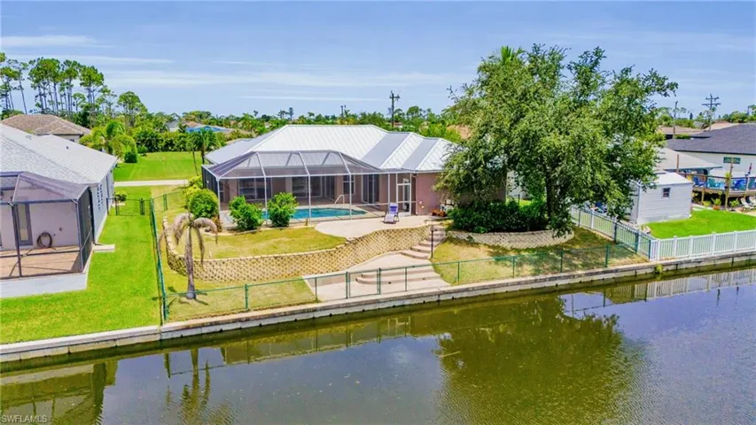 Back of property featuring a patio, a water view, a lawn, and glass enclosure