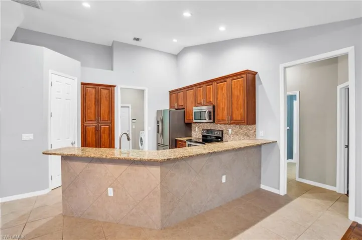 Kitchen featuring appliances with stainless steel finishes, light stone counters, kitchen peninsula, decorative backsplash, and light tile patterned flooring