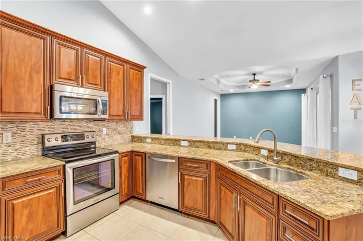 Kitchen with light tile floors, kitchen peninsula, ceiling fan, appliances with stainless steel finishes, and sink
