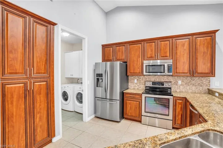 Kitchen featuring washer and clothes dryer, light tile patterned floors, light stone counters, appliances with stainless steel finishes, and decorative backsplash