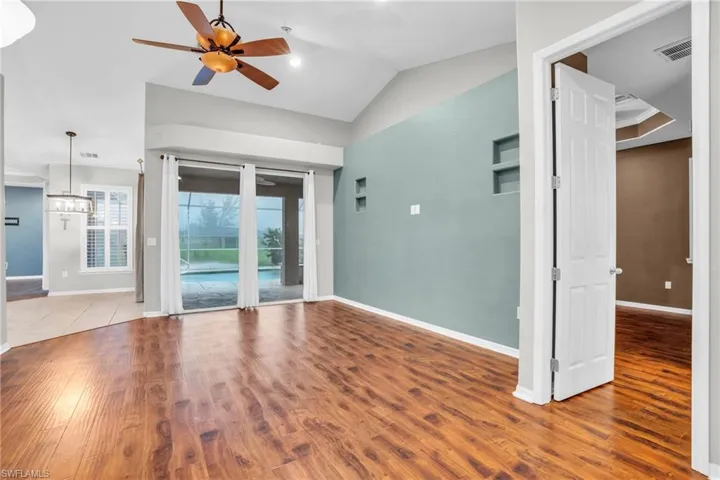 Empty room featuring ceiling fan with notable chandelier, lofted ceiling, and hardwood / wood-style floors