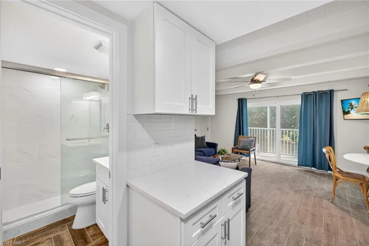 Kitchen featuring wood finish floors, white cabinetry, light stone counters, beamed ceiling, and backsplash