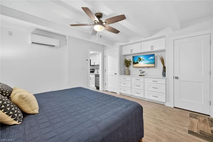 Bedroom with beamed ceiling, light wood-style flooring, ceiling fan, and a wall unit AC