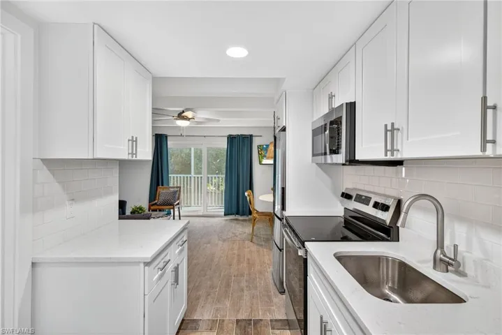 Kitchen featuring decorative backsplash, appliances with stainless steel finishes, light stone counters, white cabinetry, and recessed lighting