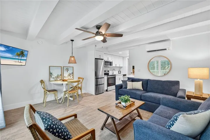 Living area featuring a wall unit AC, ceiling fan, beam ceiling, and light wood-type flooring