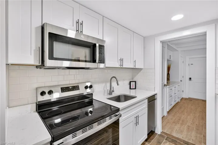 Kitchen featuring stainless steel appliances, white cabinetry, light stone countertops, backsplash, and recessed lighting