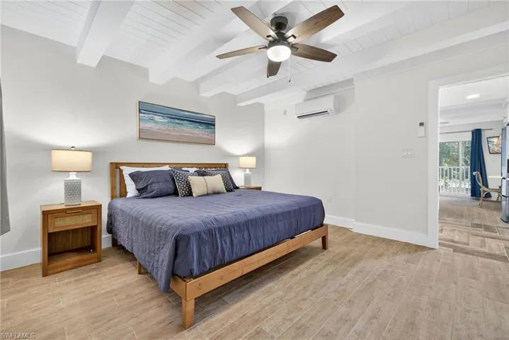 Bedroom with light wood finished floors, beam ceiling, a ceiling fan, and an AC wall unit