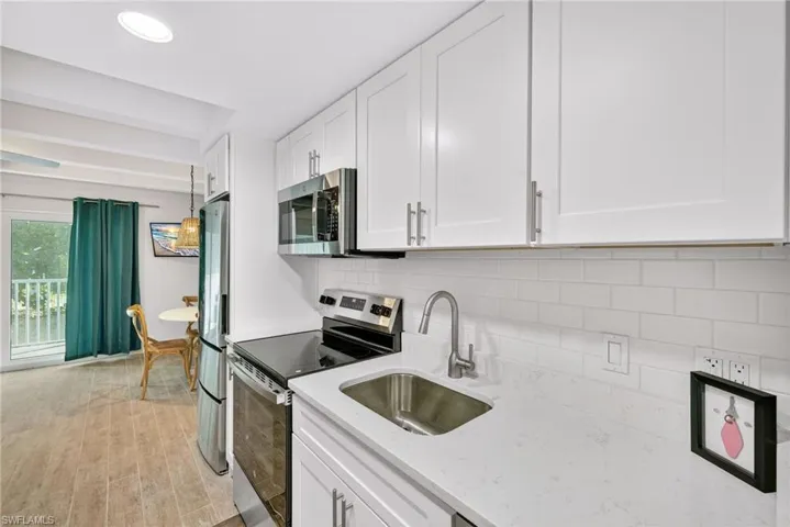 Kitchen with stainless steel appliances, decorative backsplash, white cabinets, light stone counters, and light wood-style flooring