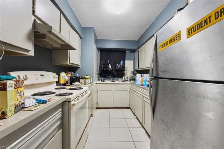 Kitchen with white range with electric stovetop, white cabinetry, sink, stainless steel fridge, and light tile patterned floors