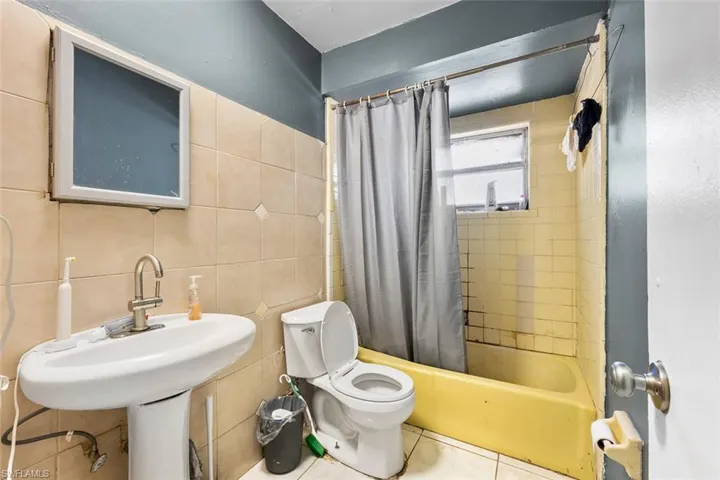 Bathroom with tile patterned flooring, tile walls, shower / bath combination with curtain, and toilet