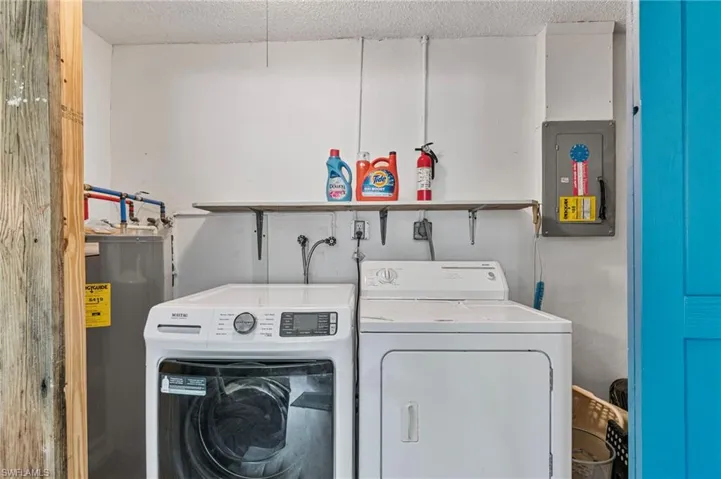 Laundry area featuring electric panel, electric water heater, washing machine and clothes dryer, and a textured ceiling