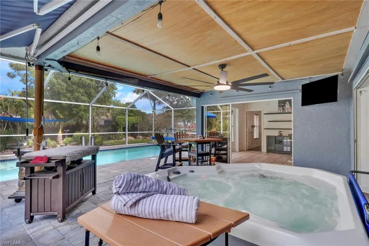 Swimming pool featuring a hot tub, a patio, outdoor dining space, glass enclosure, and a sunroom