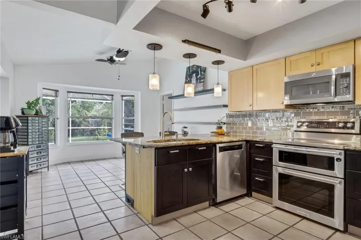 Kitchen with stainless steel appliances, decorative backsplash, light stone counters, light tile patterned floors, and pendant lighting