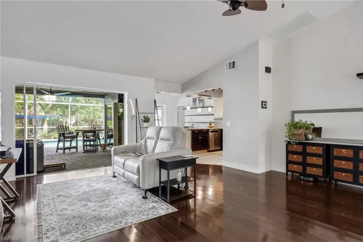 Living area with ceiling fan, dark wood-style flooring, lofted ceiling, and a sunroom