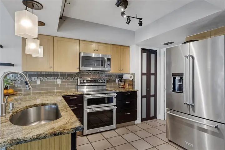Kitchen featuring stainless steel appliances, pendant lighting, light stone countertops, light tile patterned floors, and light wood finish cabinetry