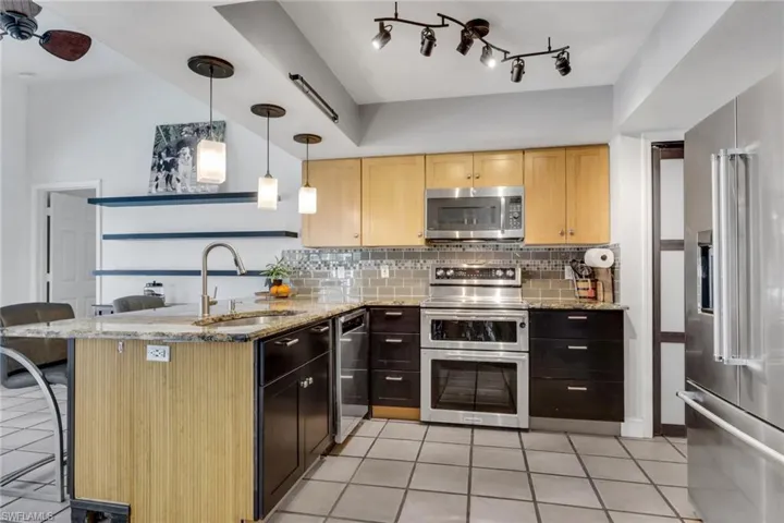 Kitchen featuring a peninsula, stainless steel appliances, a breakfast bar, light tile patterned floors, and light stone counters