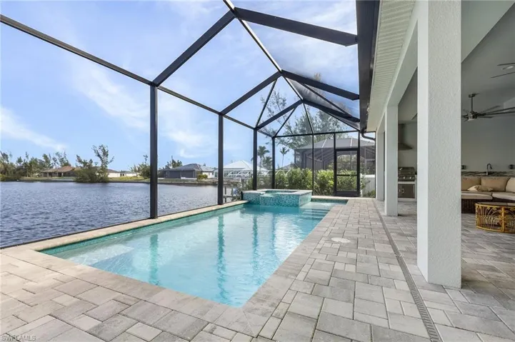 View of pool featuring an in ground hot tub, glass enclosure, a patio, ceiling fan, and a water view