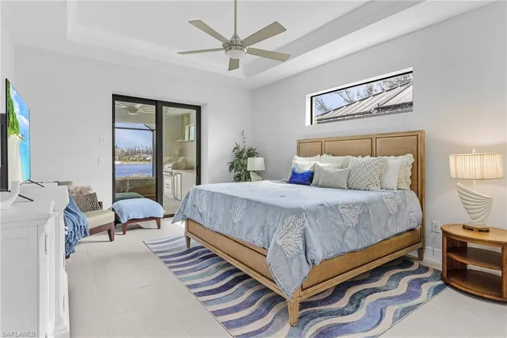 Bedroom with a tray ceiling, multiple windows, access to outside, and ceiling fan