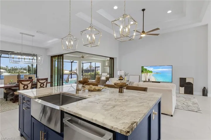 Kitchen with a center island with sink, blue cabinets, stainless steel dishwasher, and decorative light fixtures