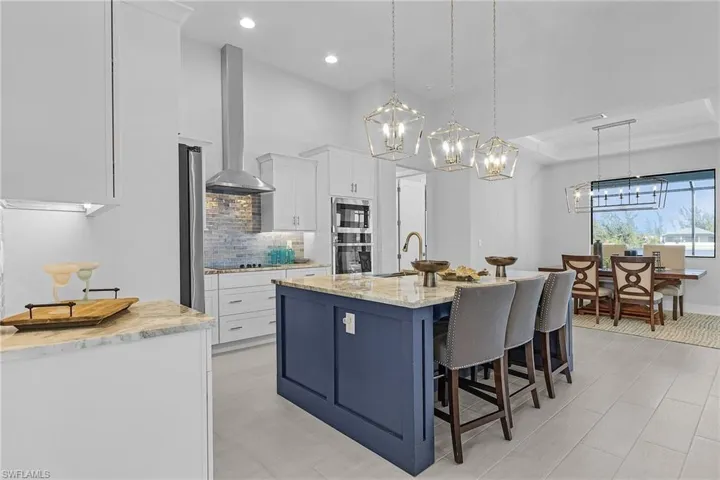 Kitchen featuring hanging light fixtures, white cabinetry, light stone countertops, a kitchen island with sink, and wall chimney exhaust hood
