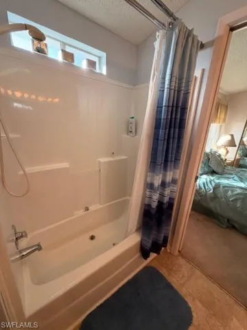 Ensuite bathroom featuring shower / bath combo, a textured ceiling, and tile patterned floors