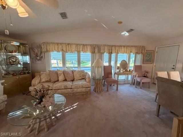 Carpeted living room featuring a textured ceiling, a ceiling fan, and vaulted ceiling